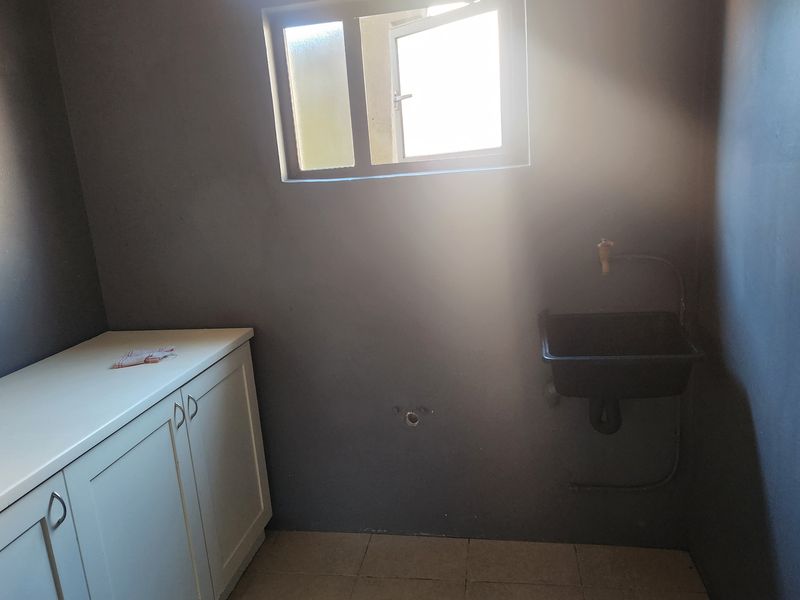 A functional laundry area featuring built-in cabinetry, a wall-mounted utility sink, and tiled flooring, providing a practical space for household tasks.