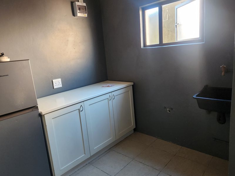 A functional laundry area featuring built-in cabinetry, a wall-mounted utility sink, and tiled flooring, providing a practical space for household tasks.