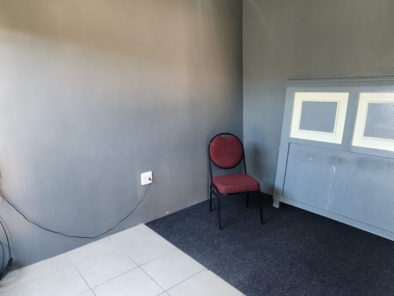 A sparsely furnished bedroom featuring a mix of tiled and carpeted flooring with grey painted walls and a single electrical outlet.
