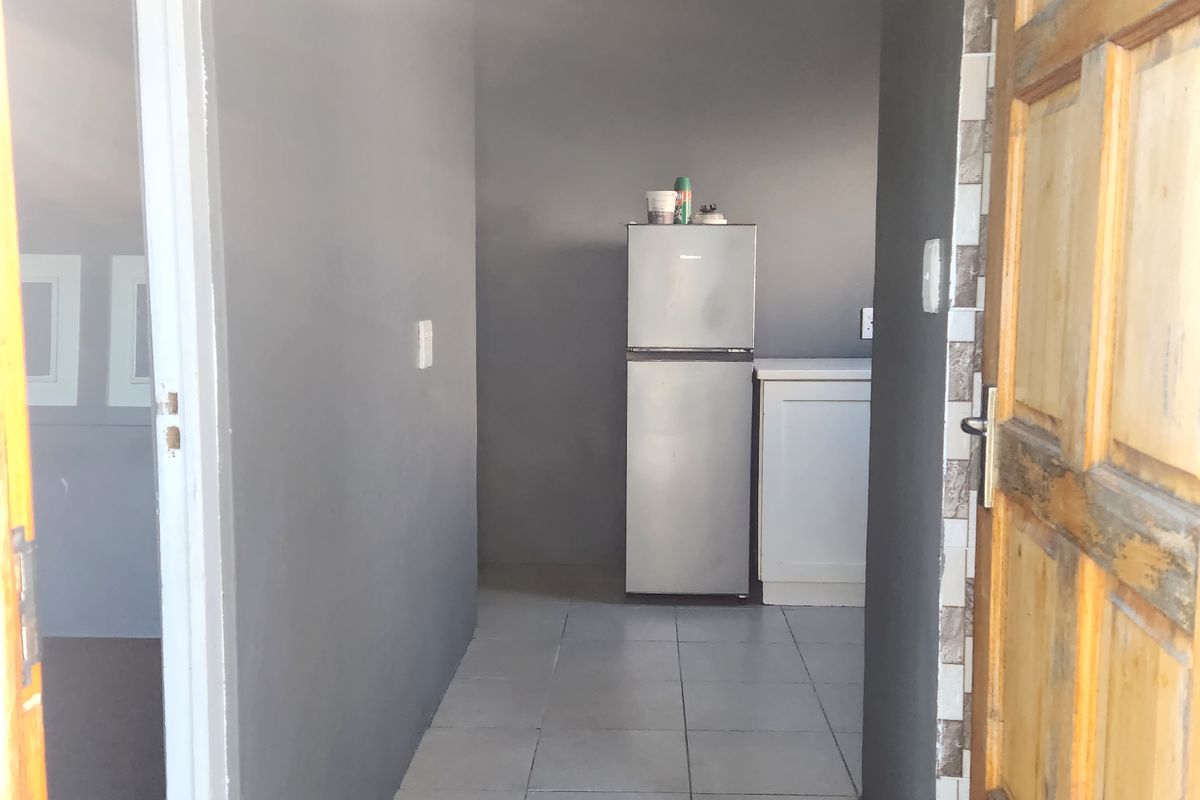 A view through a doorway into a small kitchen area featuring tiled flooring and basic built-in cabinetry.