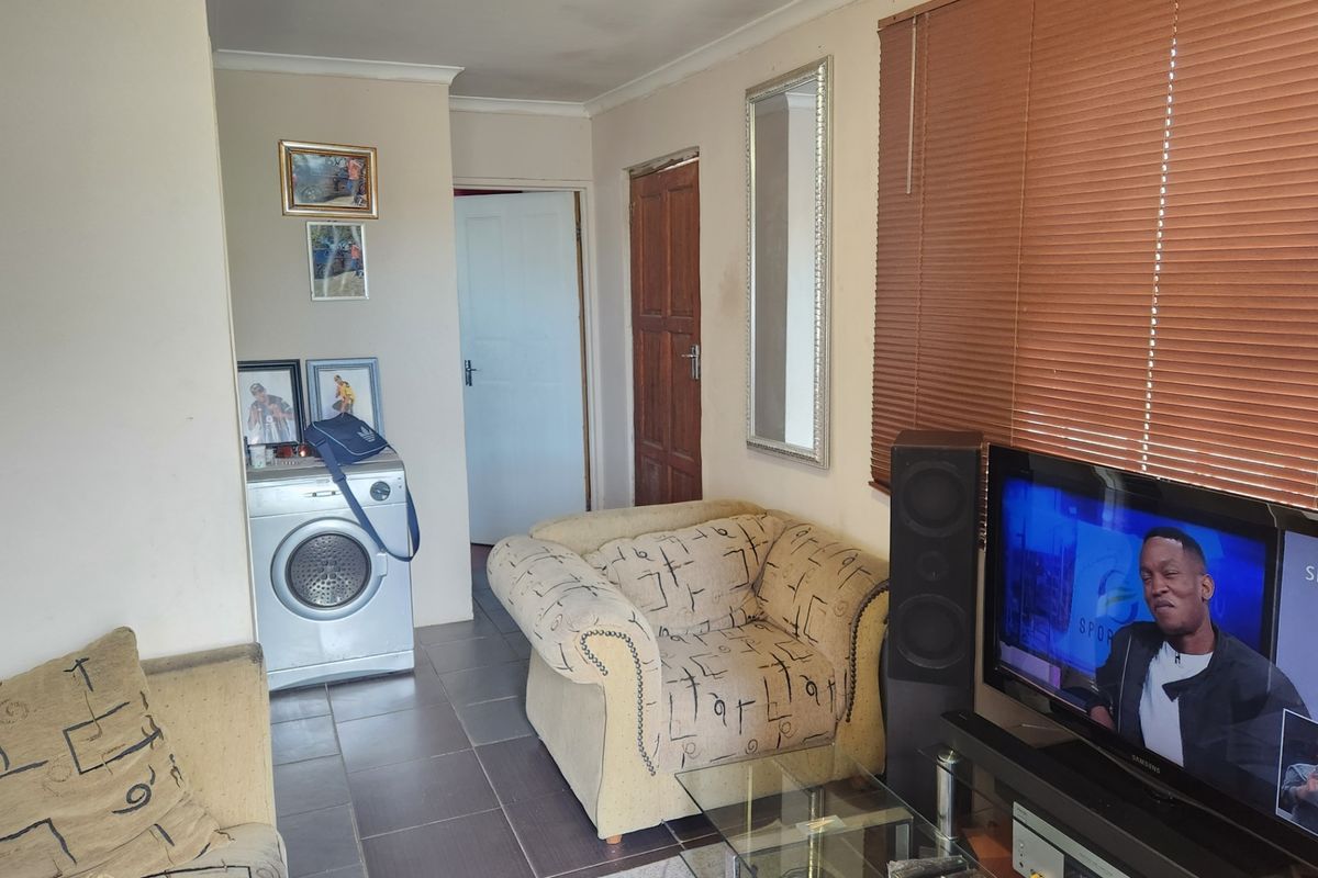A living room featuring tiled flooring, coving, and venetian blinds, providing a functional space with direct access to adjacent areas.