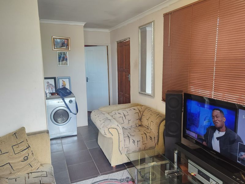 A living room featuring tiled flooring, coving, and venetian blinds, providing a functional space with direct access to adjacent areas.