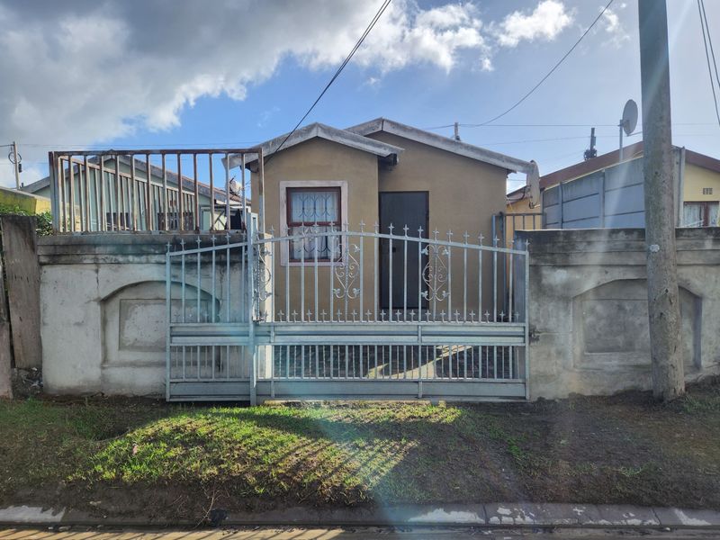 Front elevation of a single-story house featuring a secure wrought iron gate and concrete boundary wall with visible weathering.