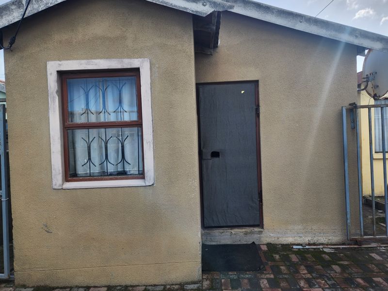 Front exterior view of the property featuring a plastered facade, security gate, and window security bars with paved ground area.