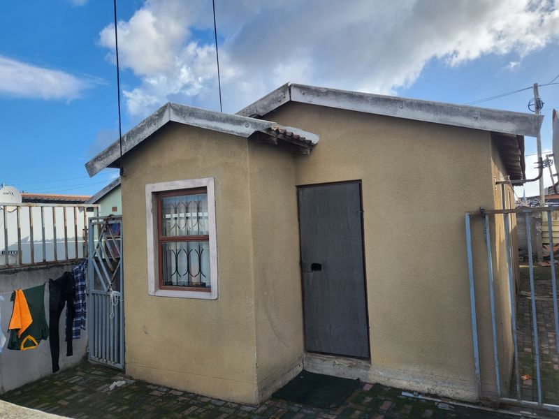 Rear view of a small outbuilding featuring a paved courtyard, security gates, and security bars on the window.