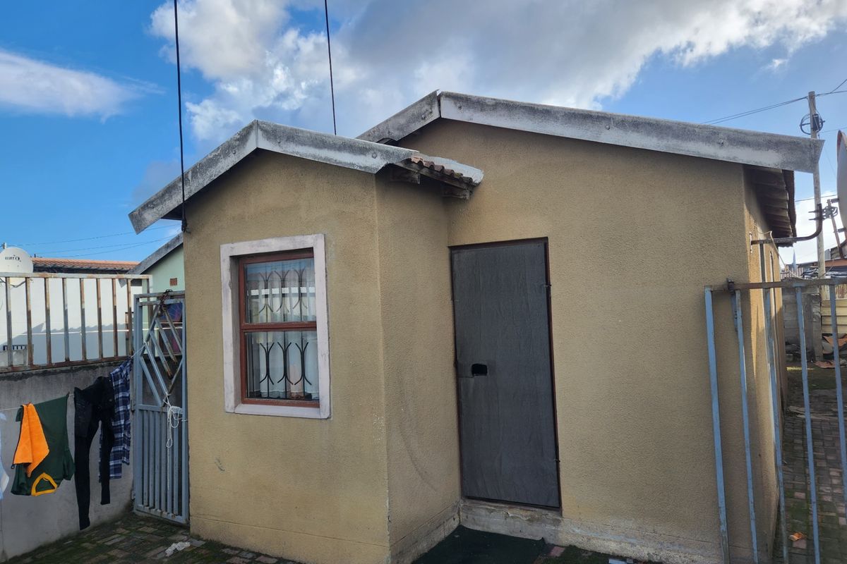 Rear view of a small outbuilding featuring a paved courtyard, security gates, and security bars on the window.