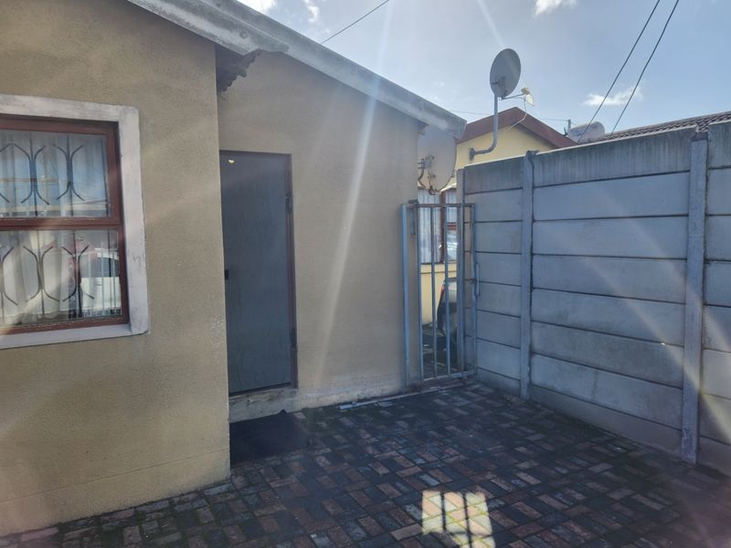 A rear exterior view showing a paved courtyard area enclosed by a precast concrete boundary wall and a side entrance door.