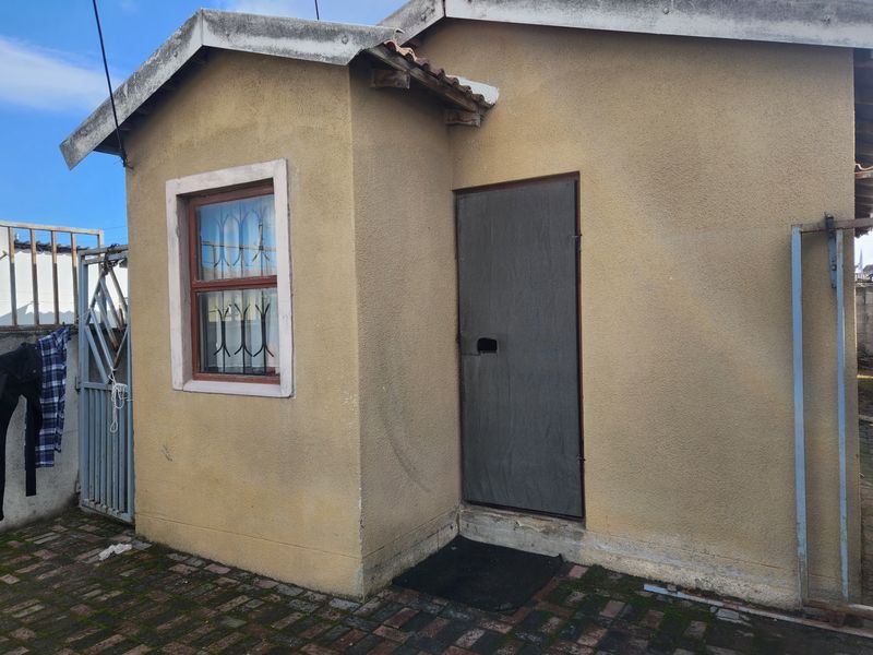 A view of the rear exterior of the property featuring a small outbuilding with security bars and a paved courtyard area.