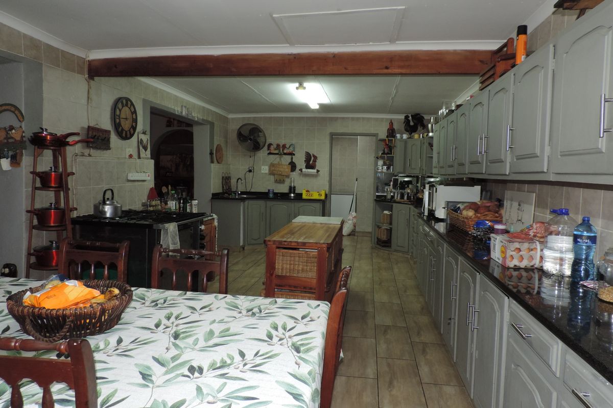 Spacious farmhouse kitchen featuring extensive built-in cabinetry, granite countertops, a gas stove, and tiled flooring with an exposed timber beam ceiling detail.