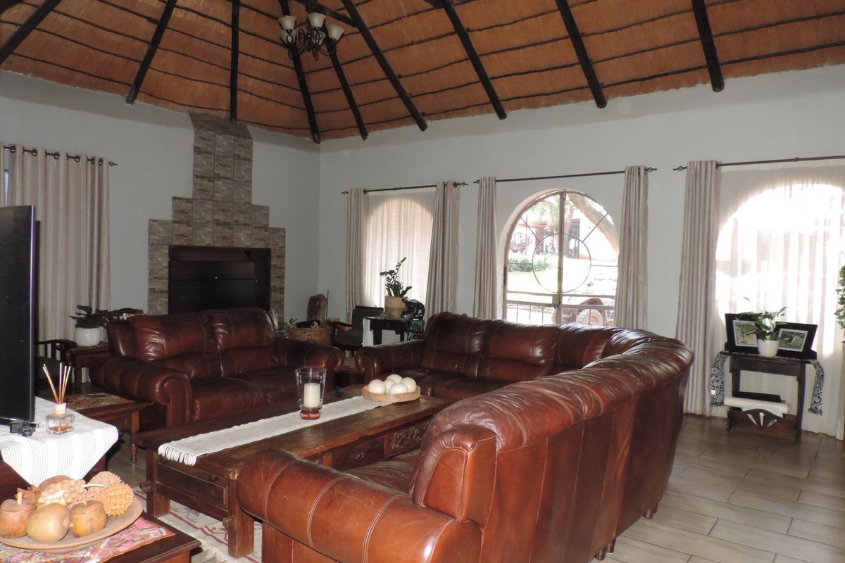 Spacious living room featuring a high vaulted thatched ceiling with exposed rafters, a stone-clad fireplace, and arched windows providing natural light.