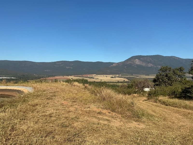 A scenic view of the expansive farm landscape featuring rolling hills and a prominent mountain range under a clear blue sky.
