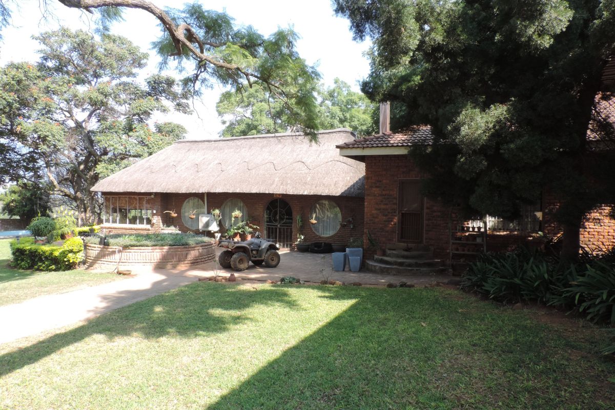 Rear view of a traditional farm-style residence featuring a thatched roof, face brick exterior, and a paved patio area set within a landscaped garden.