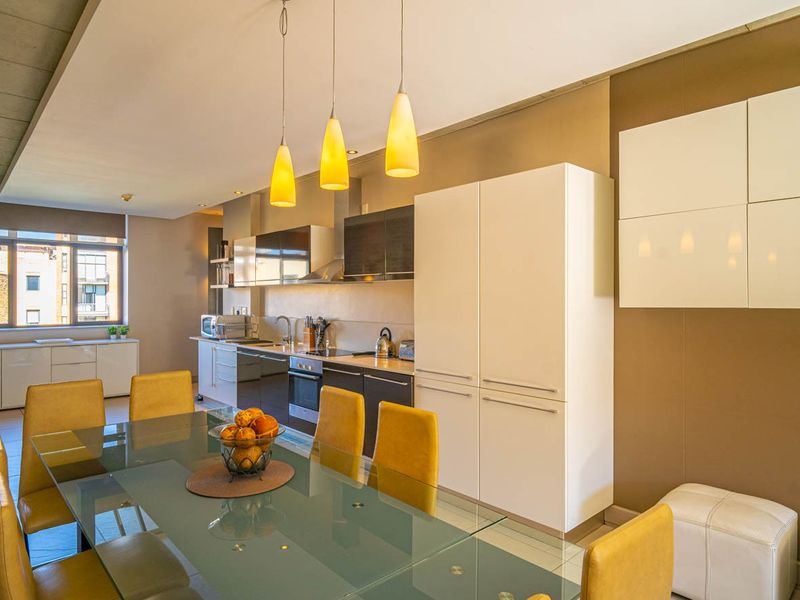 Modern open-plan kitchen and dining area featuring sleek built-in cabinetry, integrated appliances, and contemporary pendant lighting in a well-maintained apartment setting.