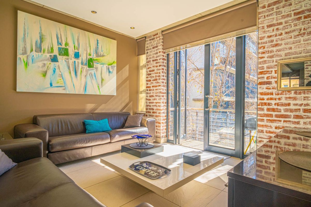 A well-lit living room featuring an exposed brick wall, large sliding glass doors leading to a balcony, and neutral tiled flooring.