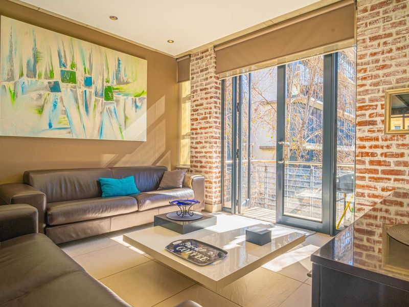 A well-lit living room featuring an exposed brick wall, large sliding glass doors leading to a balcony, and neutral tiled flooring.
