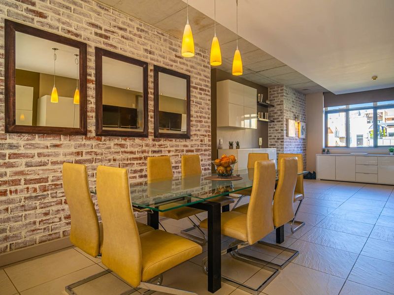 Spacious open-plan dining and living area featuring an exposed brick feature wall, modern pendant lighting, and neutral tiled flooring throughout.
