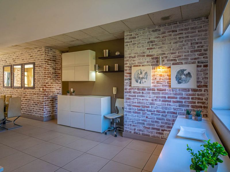 Spacious open-plan living area featuring exposed brick walls, neutral tiled flooring, and modern built-in cabinetry, offering a contemporary industrial aesthetic.