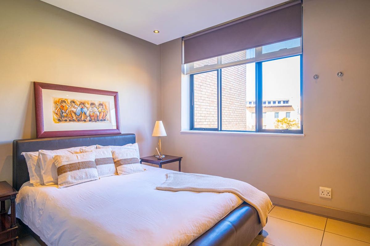 A well-maintained bedroom featuring tiled flooring, recessed downlighting, a built-in wardrobe, and a large window with a fitted roller blind.