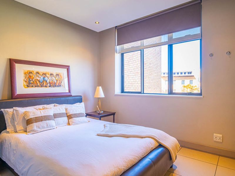 A well-maintained bedroom featuring tiled flooring, recessed downlighting, a built-in wardrobe, and a large window with a fitted roller blind.