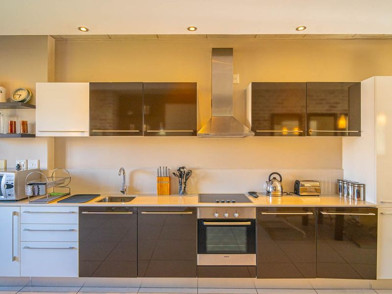 Modern kitchen featuring high-gloss cabinetry, stainless steel appliances including a built-in oven and extractor fan, and clean tiled flooring.