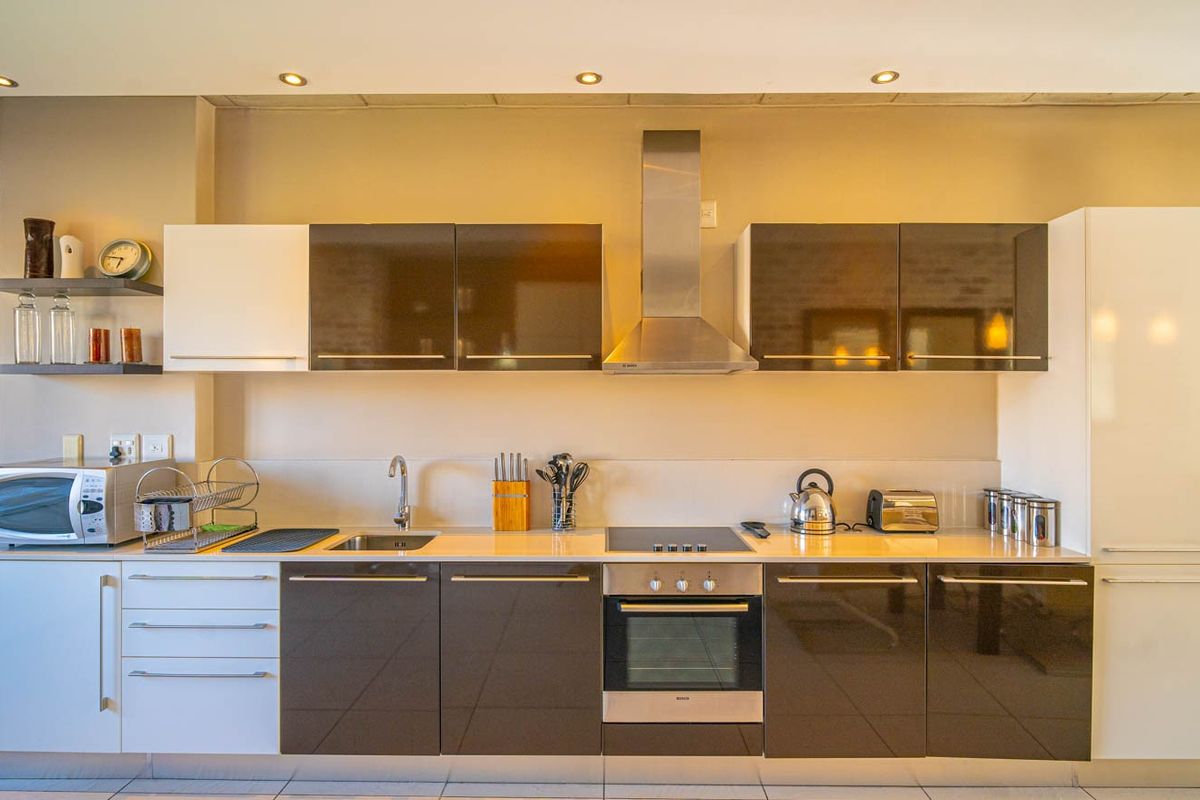 Modern kitchen featuring high-gloss cabinetry, stainless steel appliances including a built-in oven and extractor fan, and clean tiled flooring.