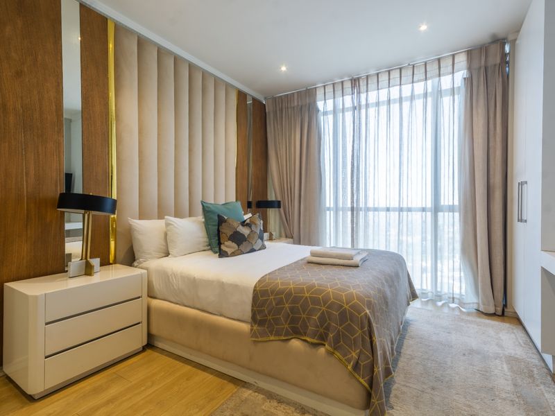 Modern bedroom featuring a custom upholstered headboard wall, built-in wardrobe, and large floor-to-ceiling windows with sheer curtains.