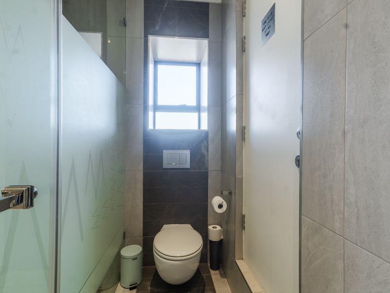 A modern bathroom featuring a wall-mounted toilet with a concealed cistern, tiled finishes, and a frosted glass shower screen.