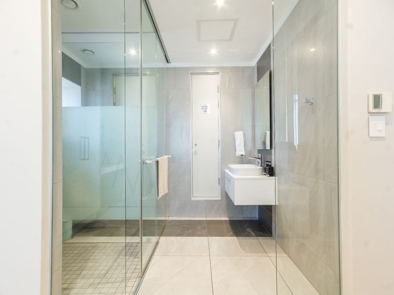 Modern bathroom featuring a glass-enclosed shower, wall-mounted vanity with basin, and neutral floor-to-ceiling tiling.