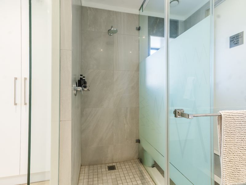 A modern bathroom featuring a walk-in shower with large format grey wall tiles, a mosaic tiled floor, and a frosted glass privacy screen.