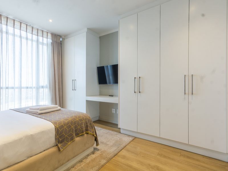 Modern bedroom featuring extensive built-in white cabinetry, a integrated desk area, laminate flooring, and large windows allowing for ample natural light.