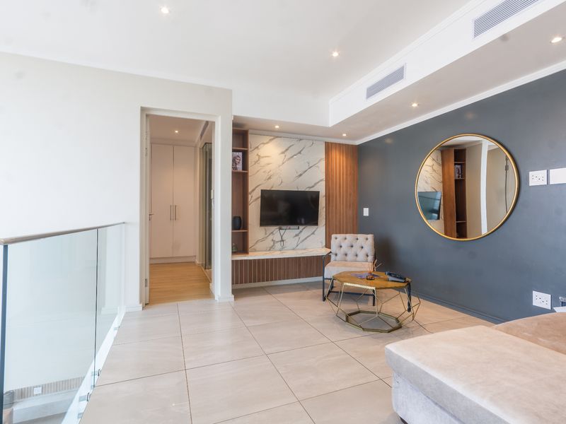 Modern living area featuring a marble-look media wall, timber accents, ducted air conditioning, and a sleek glass balustrade overlooking the lower level.