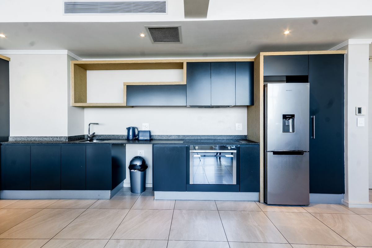 Modern kitchen featuring dark cabinetry, granite countertops, integrated stainless steel appliances, and tiled flooring with recessed lighting.