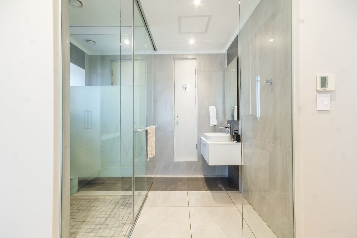 Modern bathroom featuring a glass-enclosed shower, wall-mounted vanity with basin, and neutral floor-to-ceiling tiling.