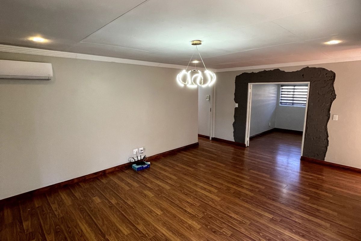 Spacious living area featuring laminate flooring, air conditioning, and modern lighting, with an unfinished decorative wall feature around the doorway.