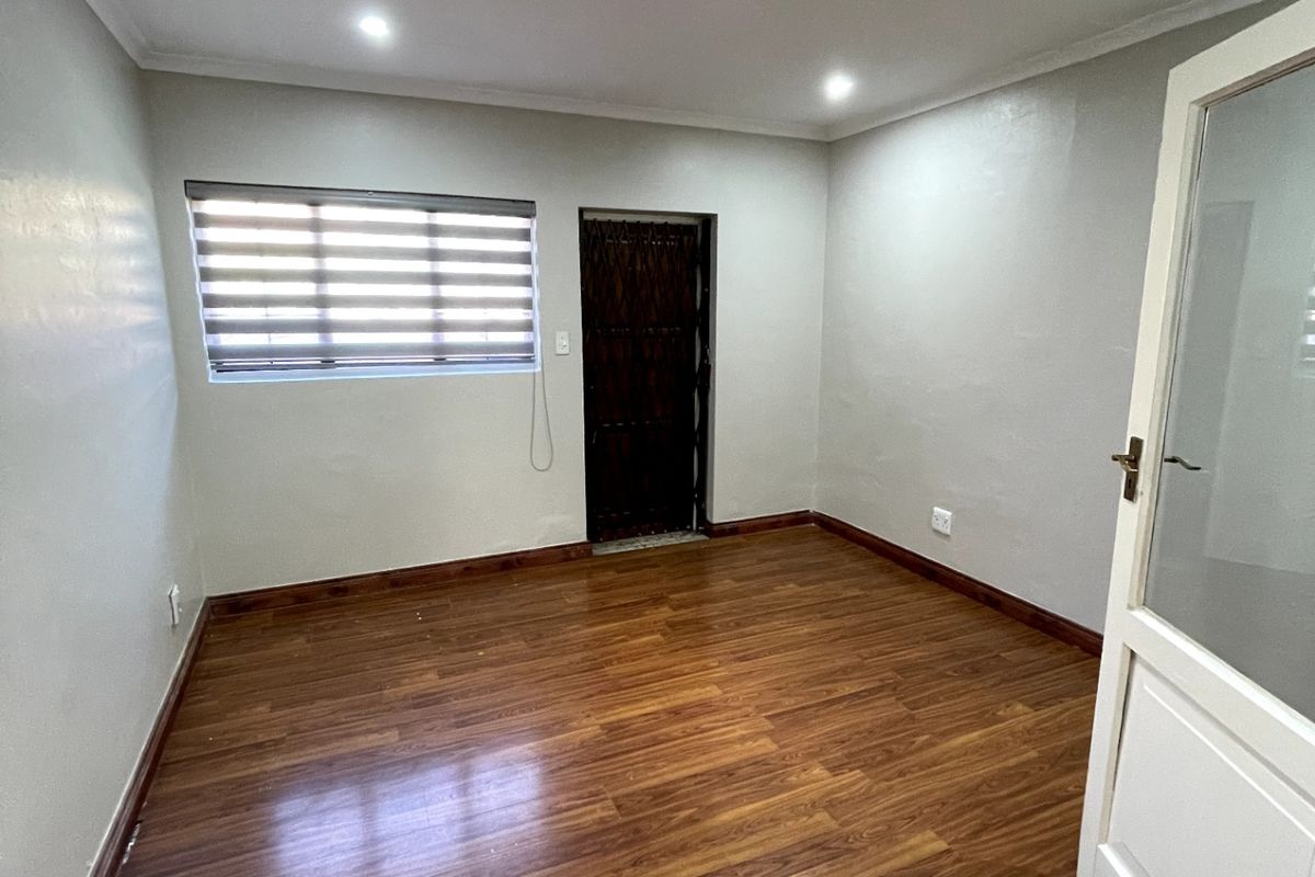 A clean, empty bedroom featuring warm-toned laminate flooring, recessed ceiling lighting, and neutral wall finishes, providing a versatile space ready for personalization.