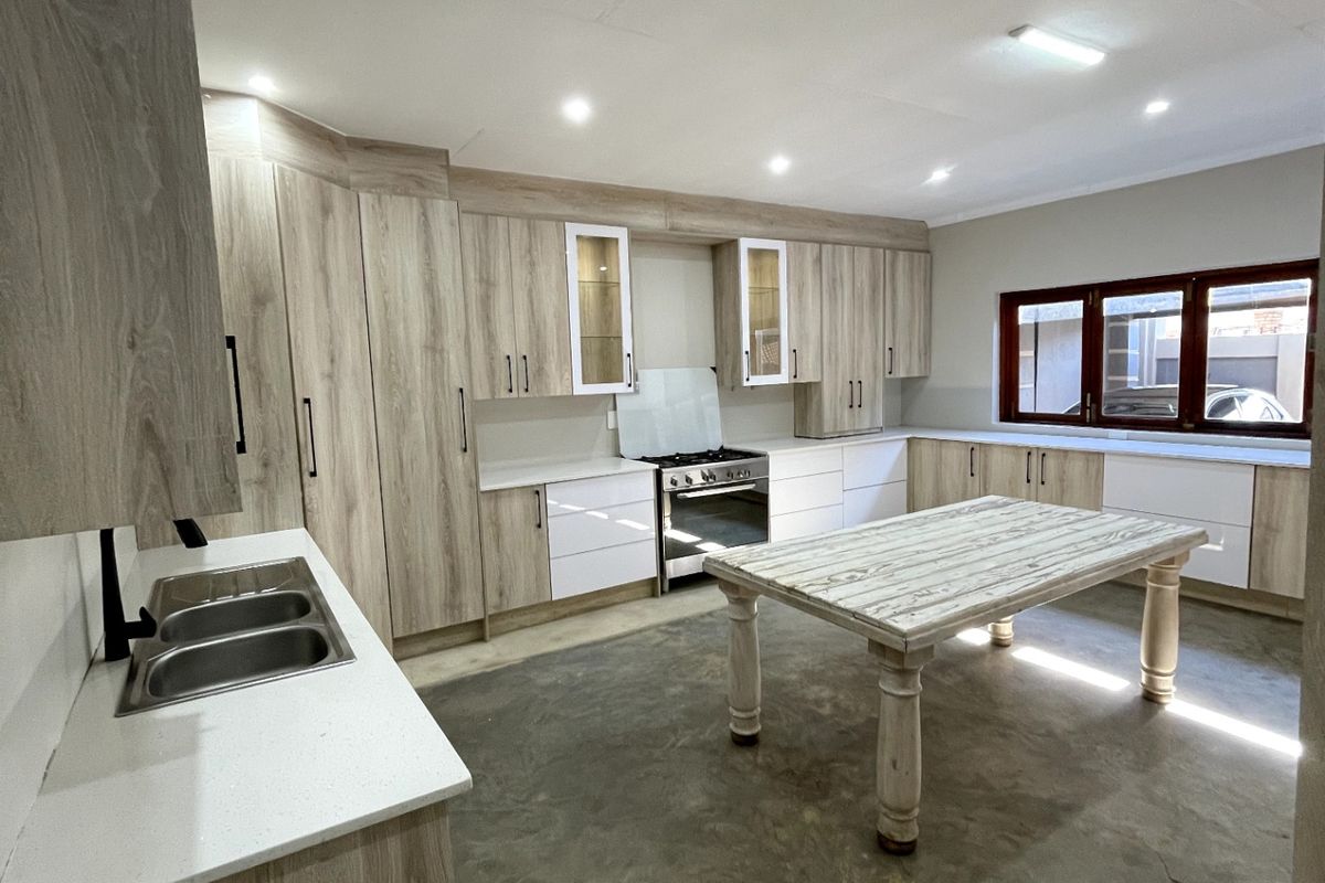 Modern kitchen featuring light wood-grain cabinetry, quartz countertops, a gas stove, and a central island, set against a concrete floor finish.