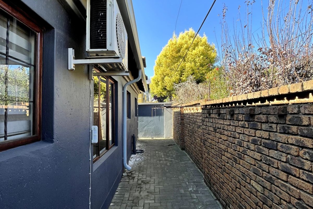 A narrow side passage featuring paved flooring, a brick boundary wall, and an externally mounted air conditioning unit.