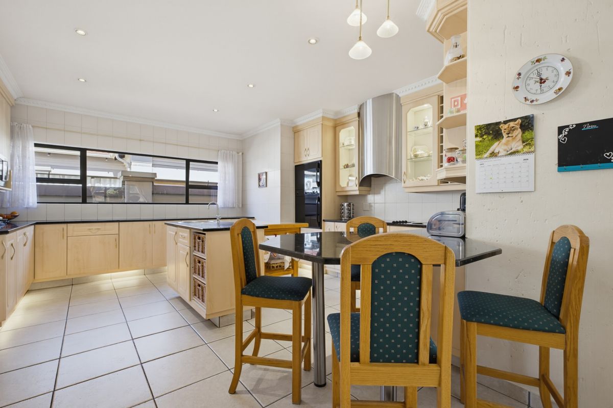 Spacious kitchen featuring light wood cabinetry, a central island with breakfast bar, tiled flooring, and integrated stainless steel appliances.