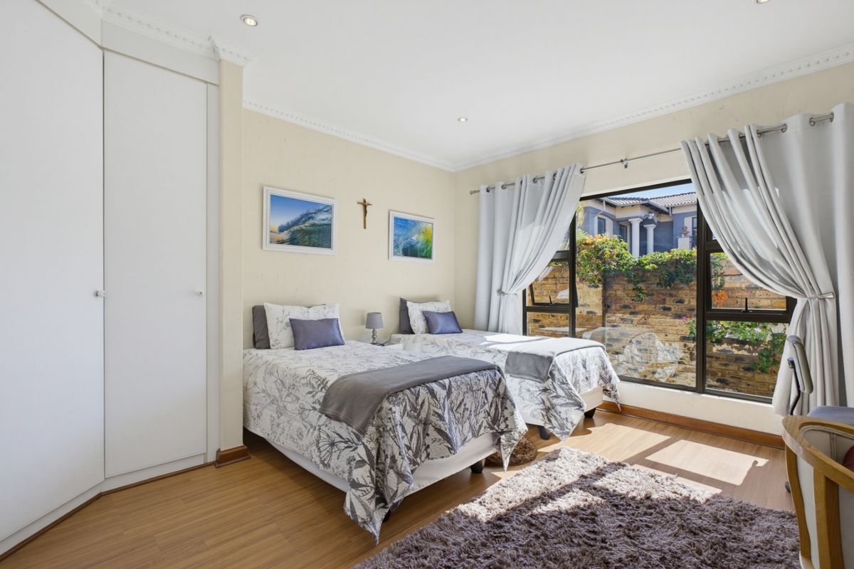 A well-maintained bedroom featuring laminate flooring, built-in cupboards, decorative cornicing, and large windows providing natural light and a view of the garden.