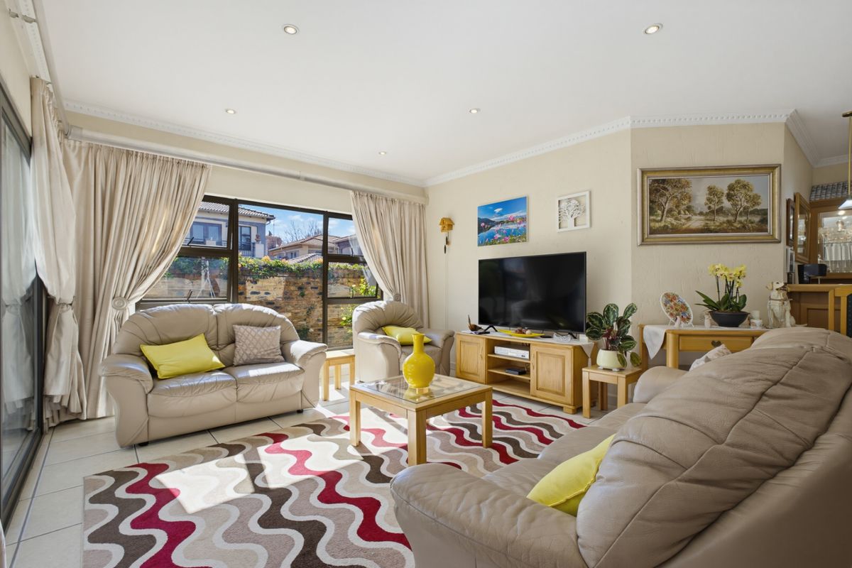 A bright and comfortable living room featuring tiled flooring, recessed downlighting, and large sliding glass doors that provide natural light and garden access.