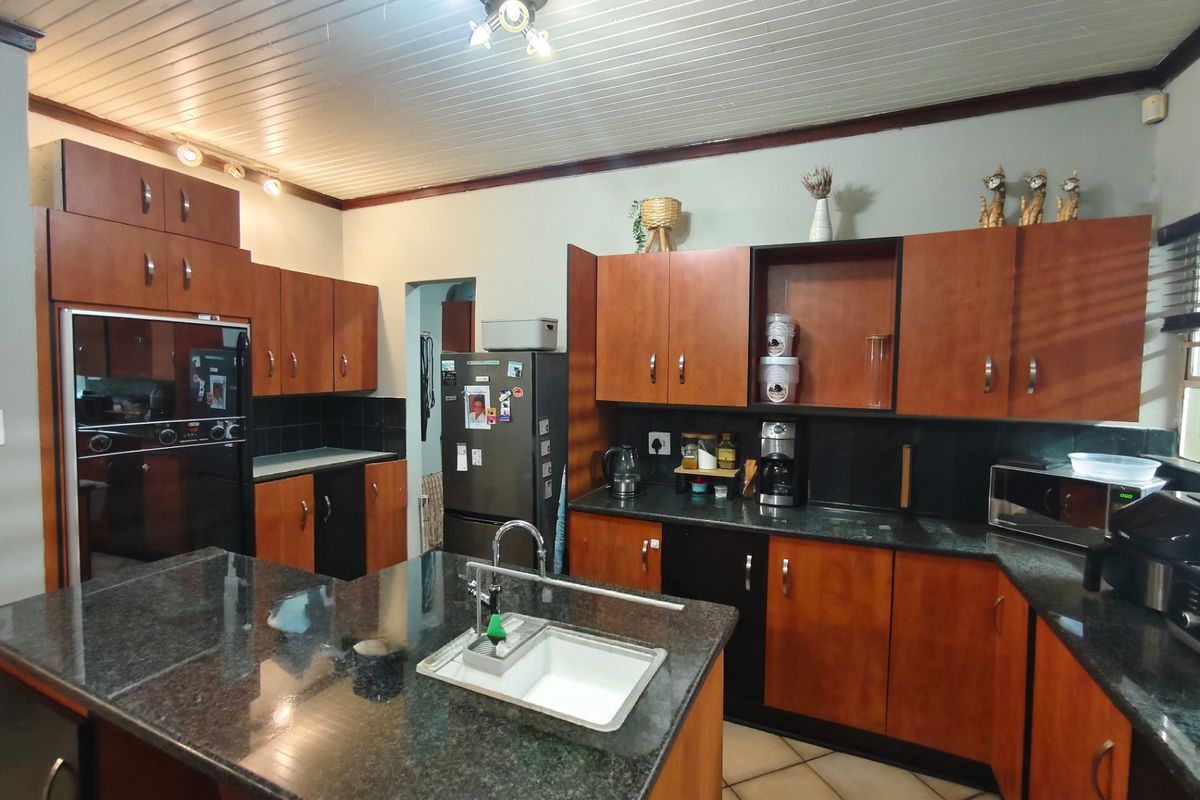 A functional kitchen featuring granite countertops, a central island with an undermount sink, built-in oven, and ample wooden cabinetry.