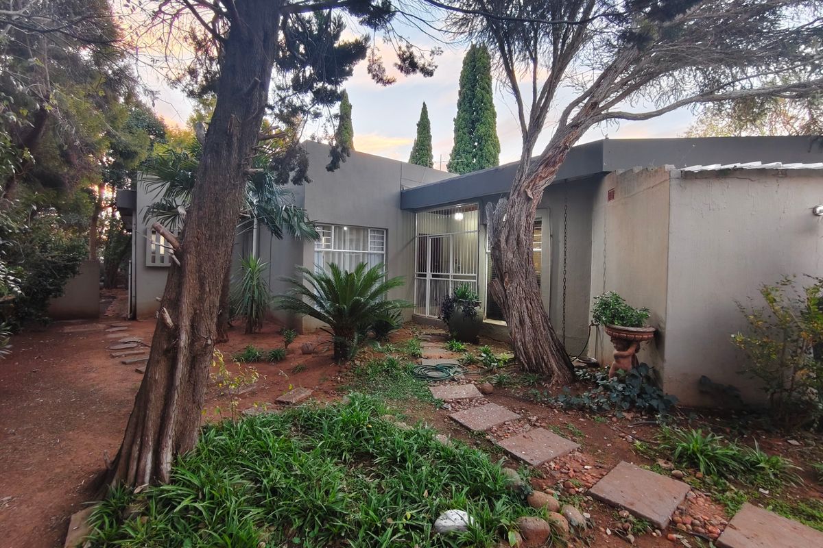 Rear exterior view of the property featuring a landscaped garden, mature trees, and a paved pathway leading to the main entrance.