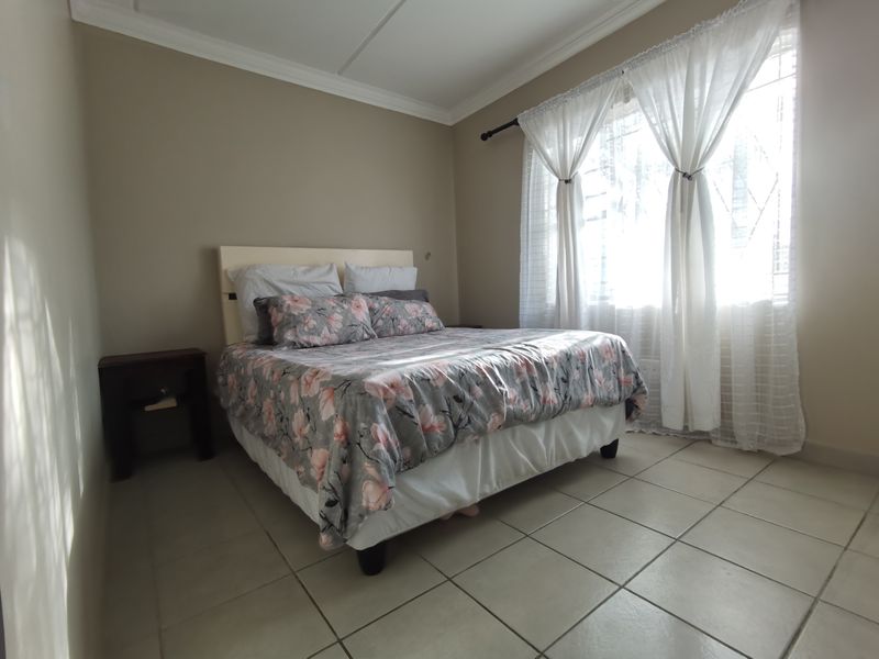 A functional bedroom featuring tiled flooring, neutral wall tones, and security bars on the window, providing a comfortable and secure living space.
