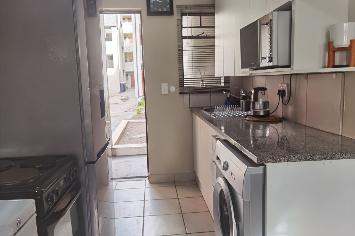 Compact kitchen featuring granite countertops, built-in cabinetry, and tiled flooring, with direct access to an exterior courtyard area.