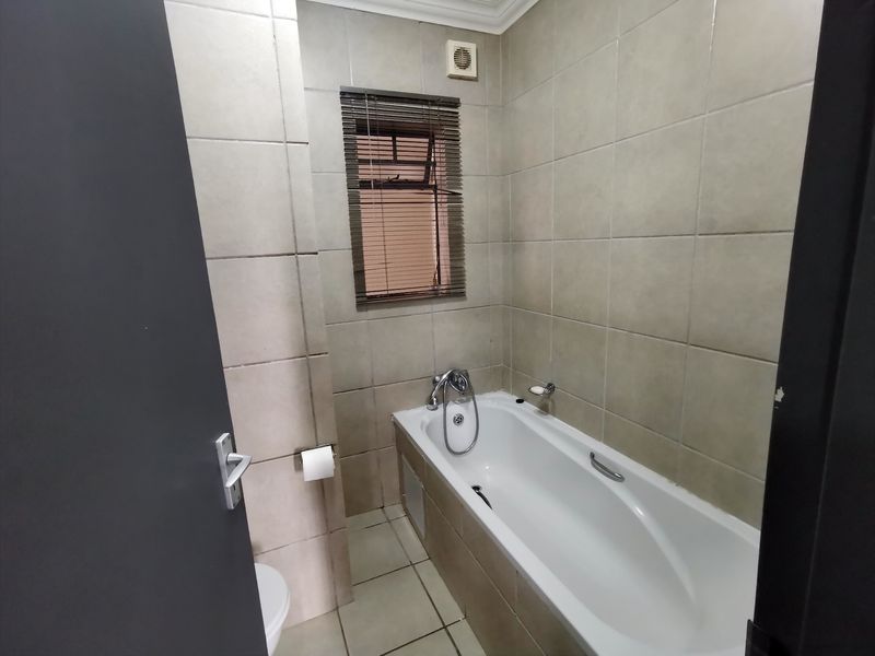 A functional bathroom featuring a bathtub with a mixer tap, tiled walls and flooring, and an integrated extractor fan.