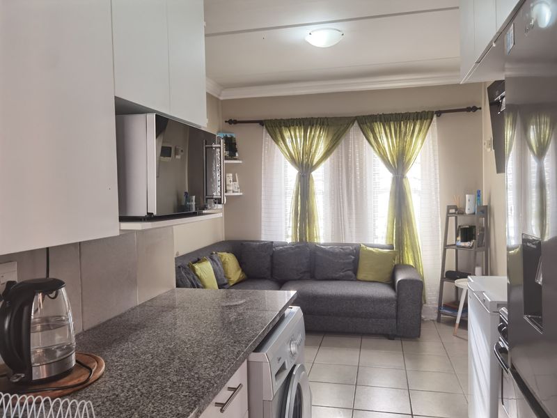 An open-plan living and kitchen area featuring granite countertops, white cabinetry, and tiled flooring, creating a functional and compact living space.