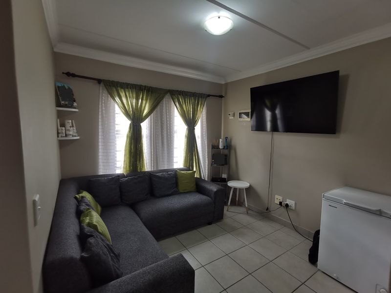 A compact living room featuring tiled flooring, neutral wall tones, and a wall-mounted television setup with integrated electrical points.