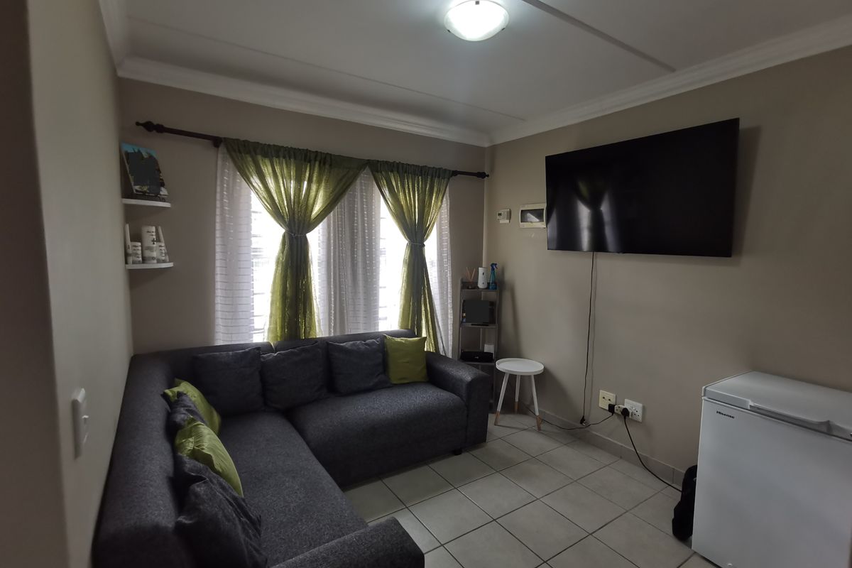 A compact living room featuring tiled flooring, neutral wall tones, and a wall-mounted television setup with integrated electrical points.