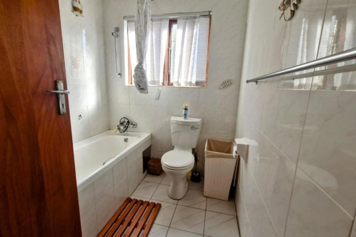 A functional bathroom featuring a bathtub, toilet, and fully tiled walls and flooring, providing a clean and practical space.