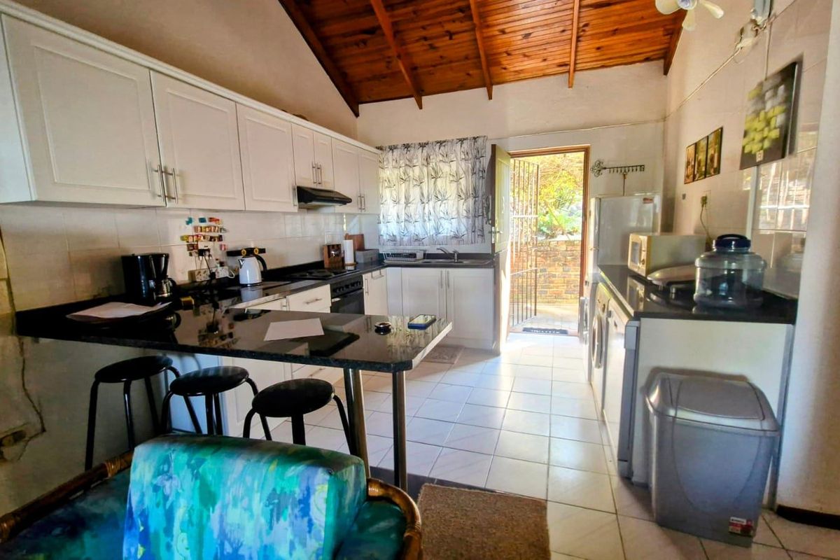 Functional kitchen featuring white cabinetry, black granite countertops, and exposed timber ceiling beams, with direct access to an outdoor area.